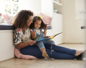 Mother sitting on the floor reading a book with her daughter