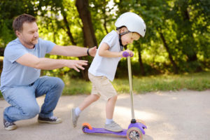 father showing his toddler son how to ride a scooter