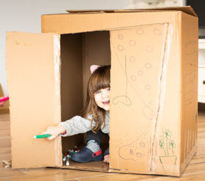 A girl looking out of a cardboard playhouse.